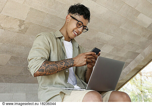 Happy freelancer using smart phone sitting with laptop