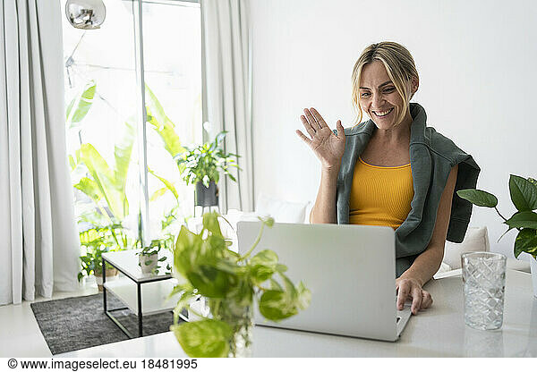 Happy freelancer waving on video call at home
