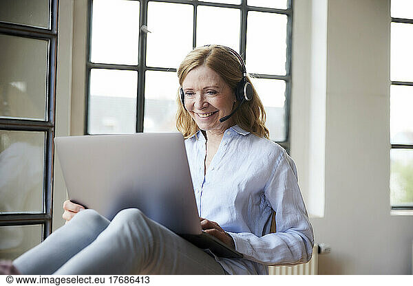 Happy freelancer wearing headset working on laptop at home