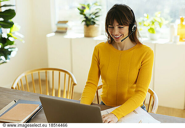 Happy freelancer wearing headset working on laptop at home office