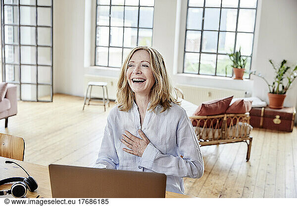 Happy freelancer with laptop sitting at table in home office