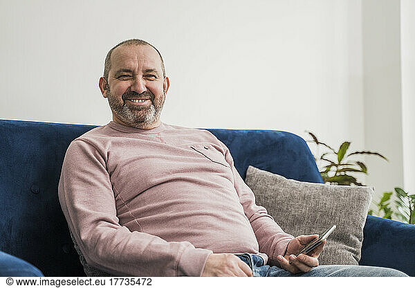Happy freelancer with smart phone sitting on sofa