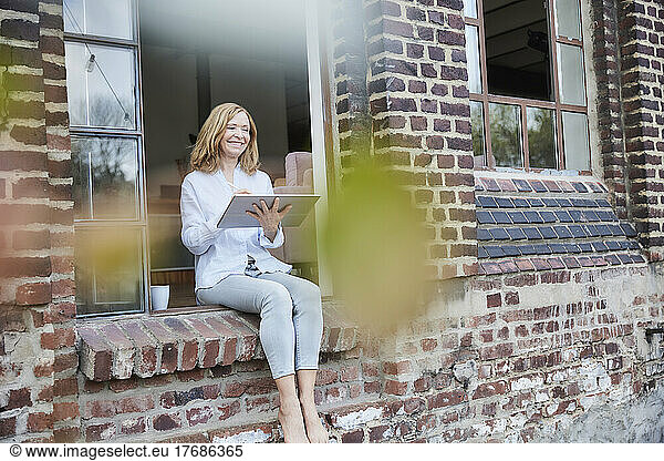 Happy freelancer with tablet PC sitting on doorway