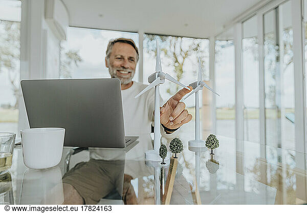 Happy freelancer with wind turbines sitting at table