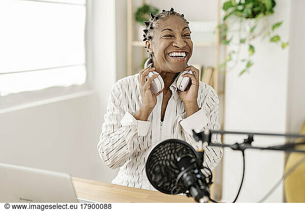 Happy freelancer with wireless headphones sitting at table in home office