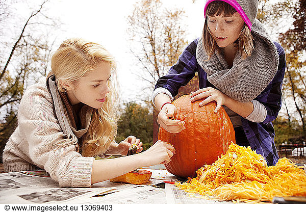 Happy friends carving Halloween pumpkin at table