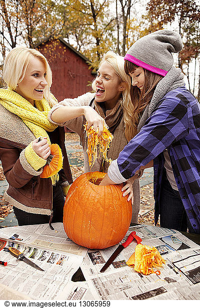 Happy friends carving pumpkin at table