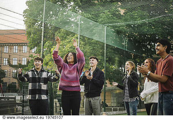 Happy friends cheering teenage girl playing basketball at court