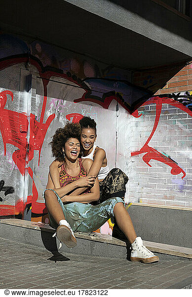 Happy friends embracing in front of graffiti wall on sunny day