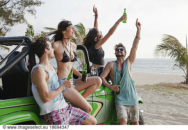 Happy friends enjoying drinks with off-road vehicle at beach