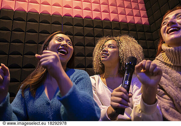 Happy friends enjoying holding microphone at amusement arcade