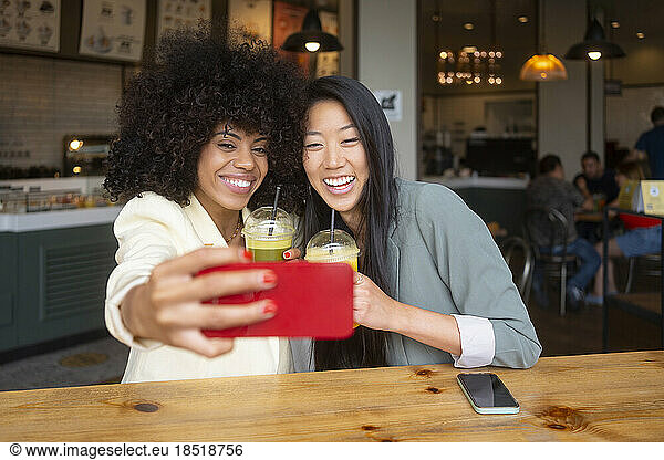 Happy friends enjoying juice taking selfie together at cafe