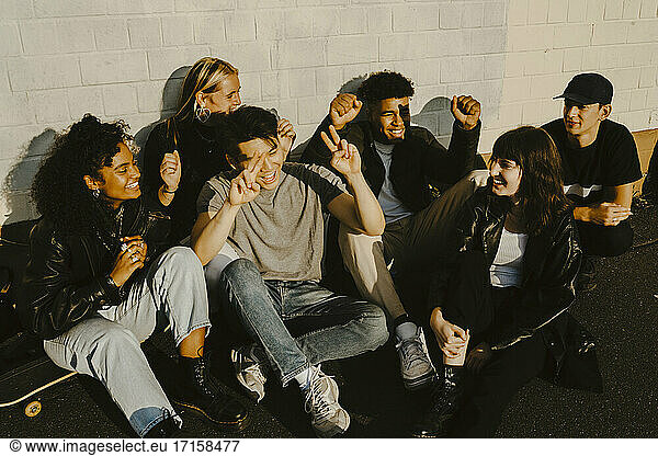 Happy friends gesturing against wall on sunny day