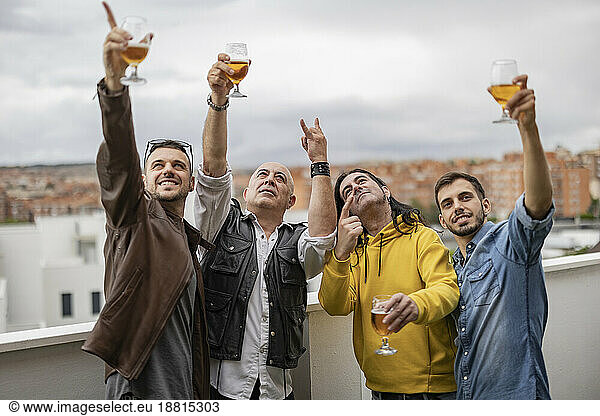 Happy friends gesturing and enjoying beer together on rooftop