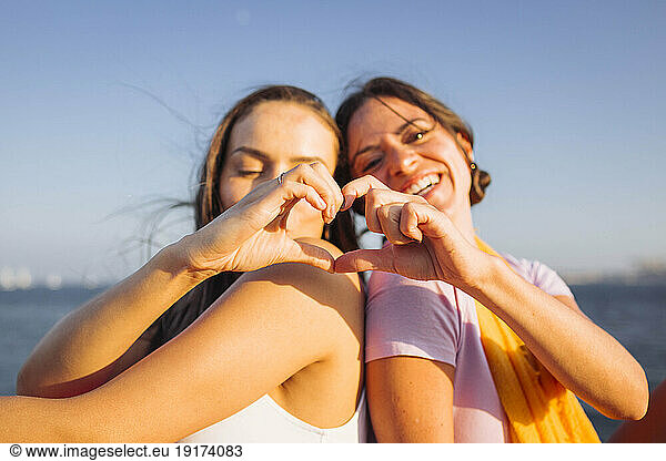 Happy friends gesturing heart shape together on sunny day