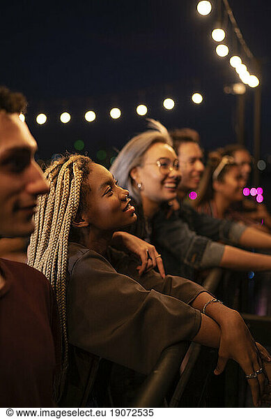 Happy friends having social gathering under string lights on rooftop