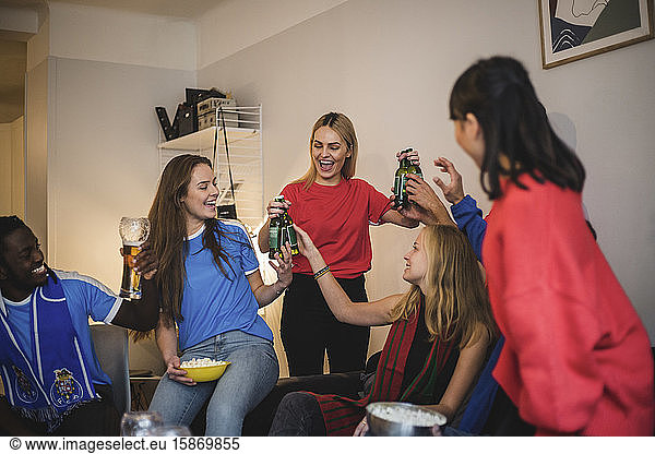 Happy friends holding beer bottles while enjoying at living room