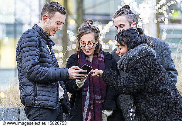 Happy friends looking at smartphone in the city
