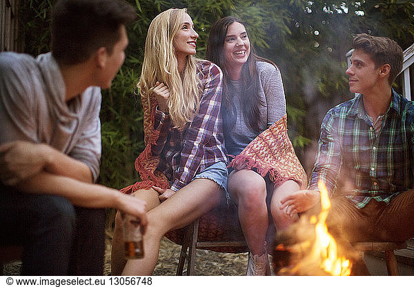 Happy friends looking away while enjoying by bonfire