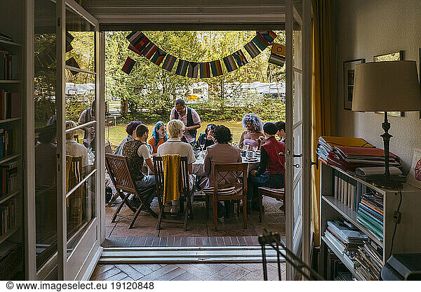 Happy friends of LGBTQ community enjoying during dinner party in back yard seen through doorway