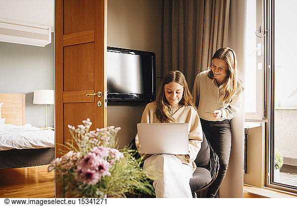 Happy friends shopping online with credit card through laptop in hotel room during vacations