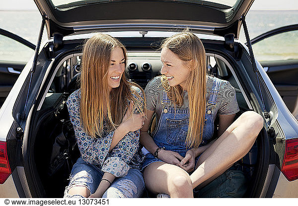 Happy friends sitting in car trunk