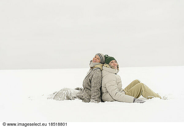 Happy friends sitting in snow in winter