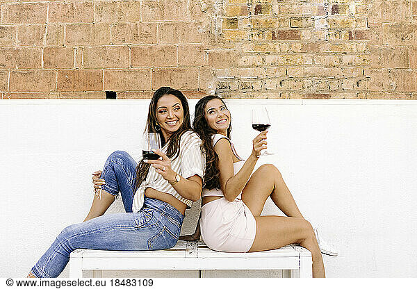 Happy friends sitting on bench with wineglasses