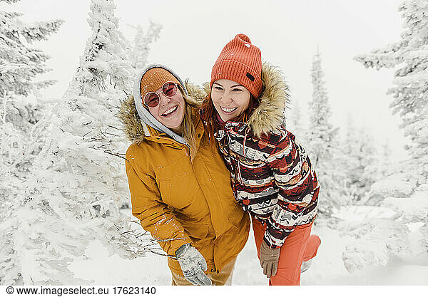Happy friends standing in winter forest on vacation
