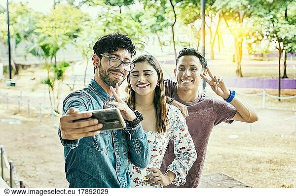 Happy friends taking a selfie in a park. Three friends standing taking a selfie in the park. Portrait of three smiling friends taking a selfie on the street. Friendship and selfie concept