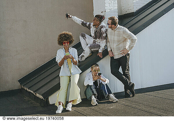 Happy friends taking selfie and using smart phones on rooftop