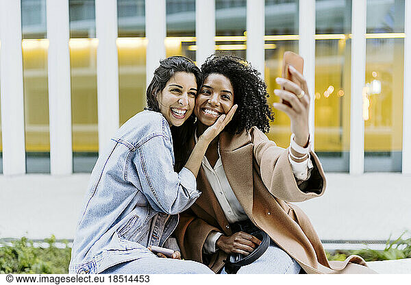 Happy friends taking selfie through smart phone in front of building