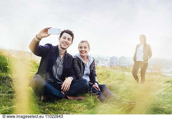 Happy friends taking selfie while sitting on grassy hill