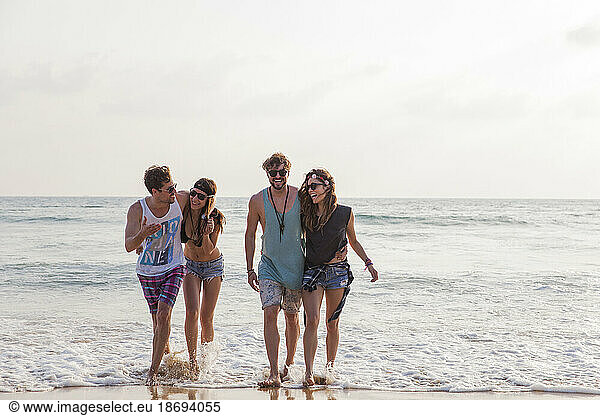 Happy friends walking in water at beach