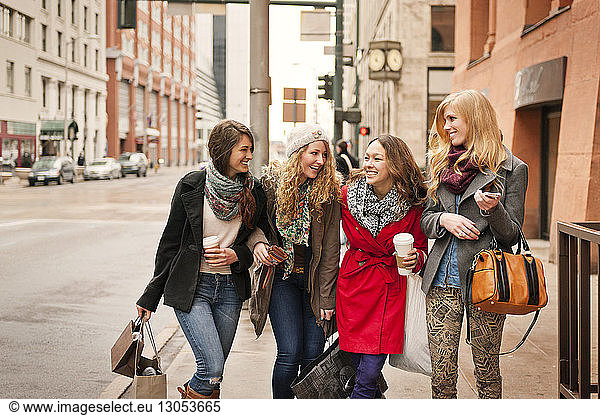Happy friends walking on sidewalk in city