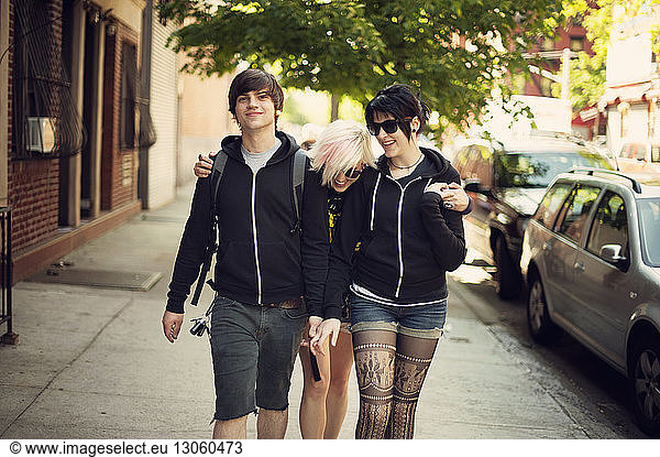 Happy friends walking on sidewalk in city