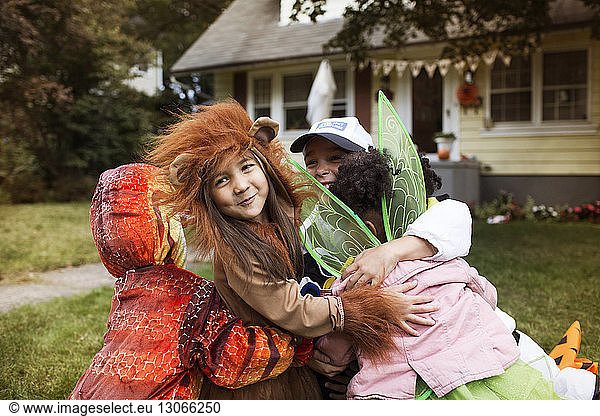 Happy friends wearing Halloween costumes embracing each other in yard