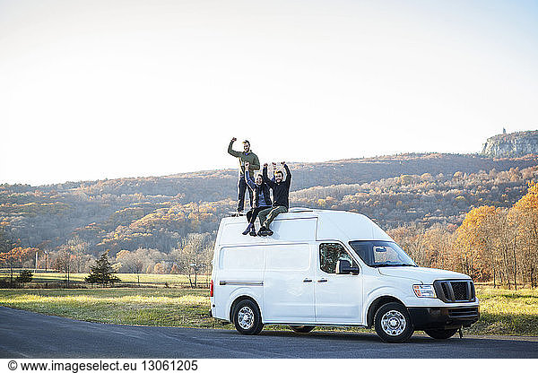 Happy friends with arms raised sitting on camper van