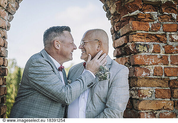Happy gay couple face to face sitting on window by brick wall