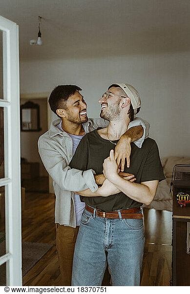 Happy gay couple looking at each other standing in bedroom at home