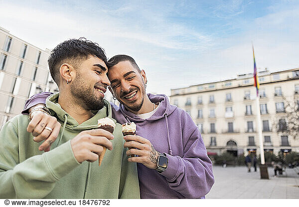 Happy gay couple with arms around holding ice cream at city street