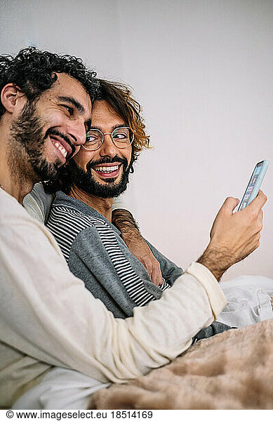 Happy gay couple with mobile phone at home
