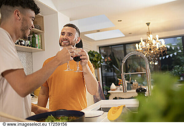 Happy gay male couple drinking wine and cooking in kitchen