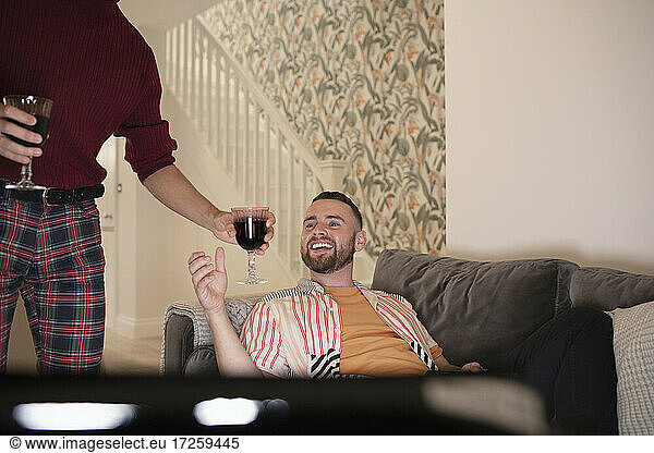 Happy gay male couple enjoying red wine and watching TV at home