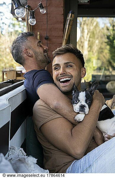 Happy gay male couple laughing while holding their French Bulldog