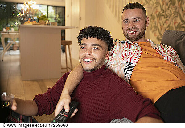 Happy gay male couple watching TV on sofa