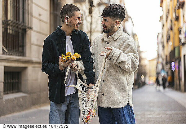 Happy gay man with boyfriend putting banana in mesh bag at street