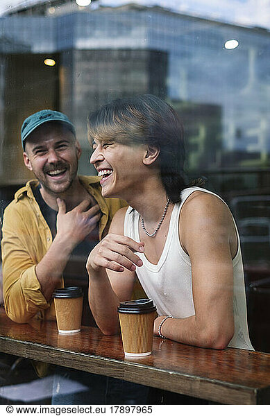 Happy gay men with coffee cups seen through window of cafe