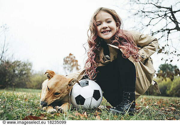 Happy girl crouching with soccer ball by dog at park