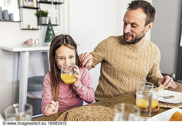 Happy girl drinking juice with father having breakfast at home
